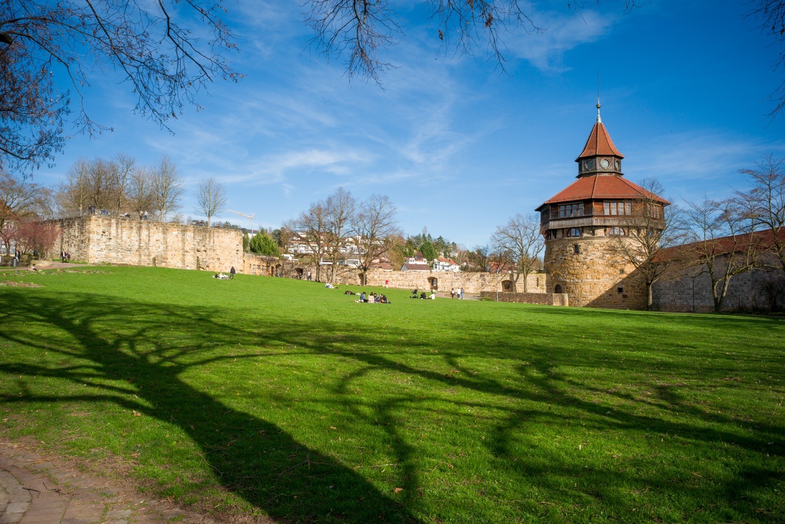 Das Foto zeigt den Burghof in #Esslingen mit dem „Dicken Turm“ im rechten Bildbereich und dem Kanonenhügel inks. Dazwischen liegt eine grüne Wiese, auf der Menschen herumliegen.