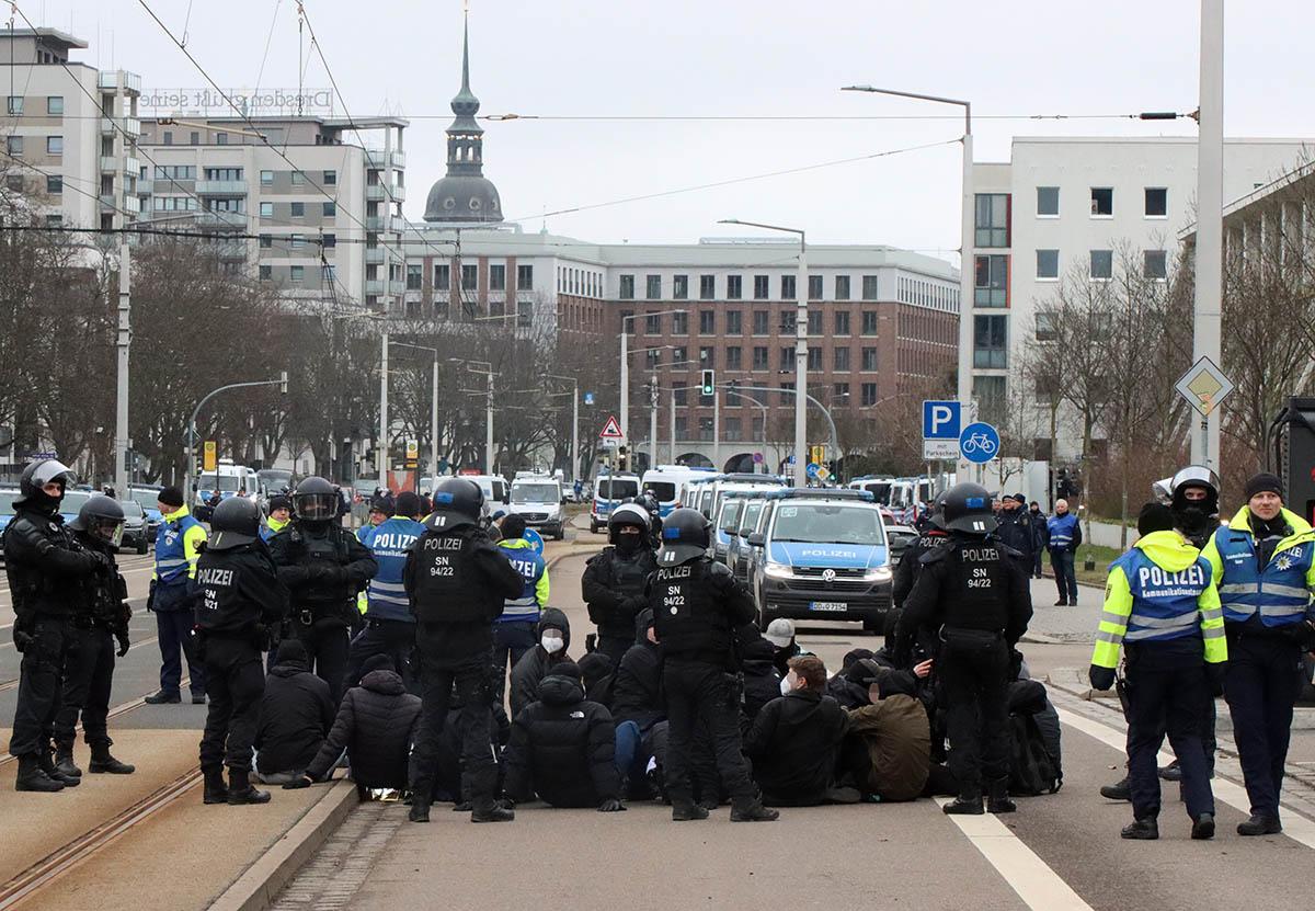 Das Foto von Kinkalitzken zeigt eine Sitzblockade, die von Bullen umstellt ist. Dahinter ist die Straße mit Wannen volgestellt. Im Hintergrund ist der Turm der Frauenkirche zu sehen.