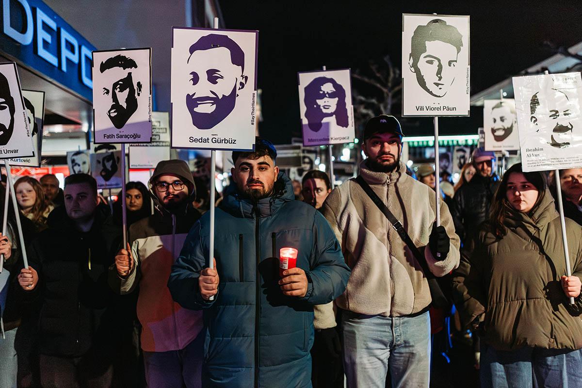 Das Foto von © Protestfotografie.Frankfurt zeigt eine Reihe Teilnehmer* der Gedenkaktionen mit stilisierten Porträts der Ermordeten und deren Namen