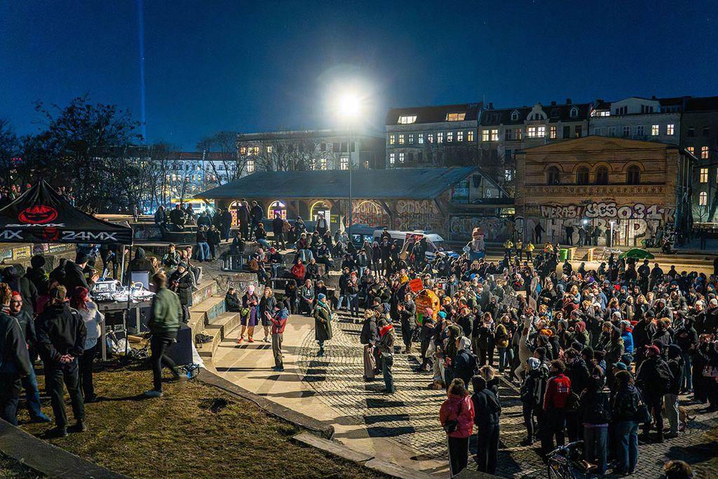 Das Foto von © Björn Obmann zeigt eine Menge Menschen am Abend auf einem Rondell, die in Richtung einer Bühne schauen