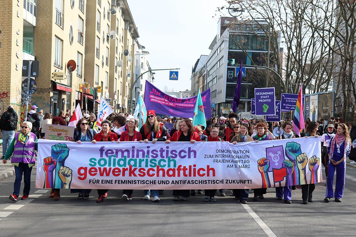 Das Foto von © Kinkalitzken zeigt das Fronttransparent mit dem Text "feministisch solidarisch gewerkschaftlich - Für eine feministische und antifaschistische Zukunft!" das von einem bunt gewürfelten Haufen Frauen* getragen wird. Dahinter weitere Transparente und Plakate.