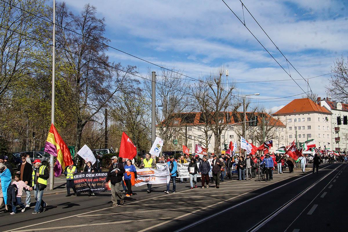 Das Foto zeigt eine Weitwinkelaufnahme eines Teils des Ostermarsches mit verschiedenen Transparenten, unter anderem Friedensglocke, DKP, IG Metall, BSW und weitere.